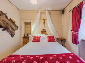 A room with a bed, a wooden headboard, a wall-mounted crucifix, a fur rug, and a curtain.