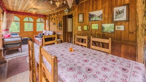 A rustic wooden room with a large table, benches, and a bed with a floral bedspread.