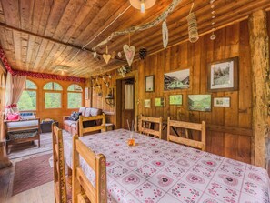 A rustic wooden room with a large table, benches, and a bed with a floral bedspread.