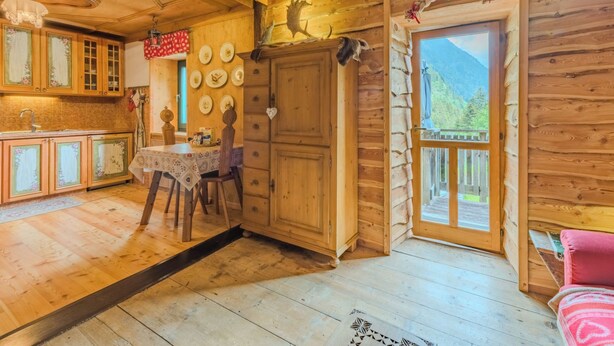 A wooden cabin interior with a dining area, kitchen, and a balcony with a mountain view.