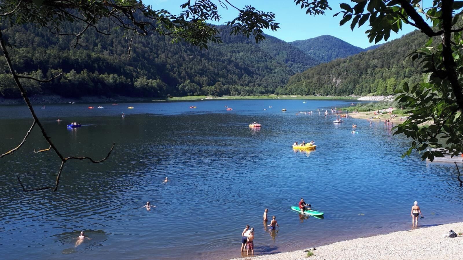 Un lago con barcos y gente, rodeado de colinas cubiertas de bosque.
