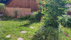 Un granero de madera con techo inclinado, rodeado de un área verde con piedras para pisar y montañas al fondo.