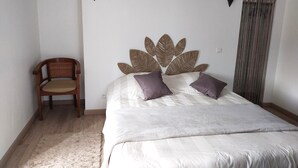 Un dormitorio con cama, una silla, un cabecero decorativo y una ventana con cortinas.