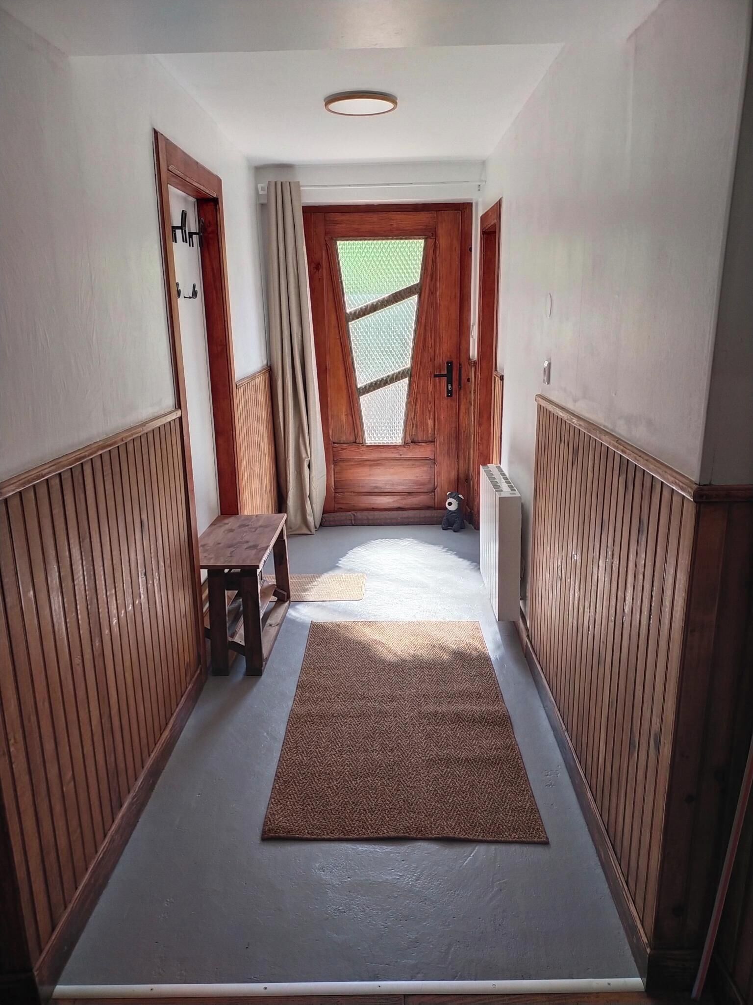 En hall med träpanel på väggarna, en bänk, en dörr med ett fönster och en matta på golvet.