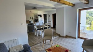Una sala de estar con un sofá, una mesa de centro y un televisor. Se ve una cocina al fondo, con un microondas, y un comedor con sillas.