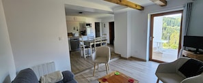 A living room with a sofa, a coffee table, and a television. There is a kitchen in the background with a microwave and a dining area with chairs. - Between Alsace and the Vosges - Les Hauts de Kruth (Kruth)