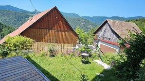 Entorno rural con dos establos de madera, un patio cubierto de césped y montañas al fondo.