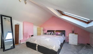 Une chambre avec un plafond en pente, un lit, une commode, un miroir et un mur en briques roses.