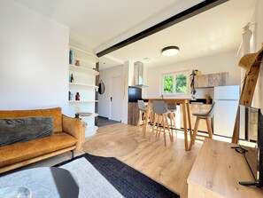 Eine moderne Küche mit Holzsärchen, einem Essbereich mit Tisch und Stühlen, einer Couch mit Kissen und einer eingebauten Schrankwand.