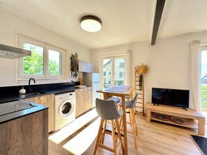 Eine moderne Küche mit Waschmaschine, einer Essecke mit Stühlen, einem Fernseher und einem großen Fenster.