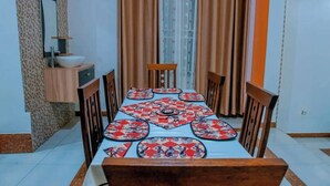 A dining area with a table set for six, a wooden cabinet with a sink, and a window with curtains.
