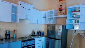 A compact kitchen with white cabinets, a stainless steel refrigerator, a gas stove, and a coffee maker.