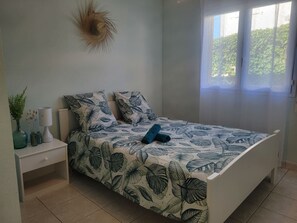 Ein Schlafzimmer mit einem Bett, Nachttischen, einer Lampe und einem Fenster mit Blick auf Grünflächen.