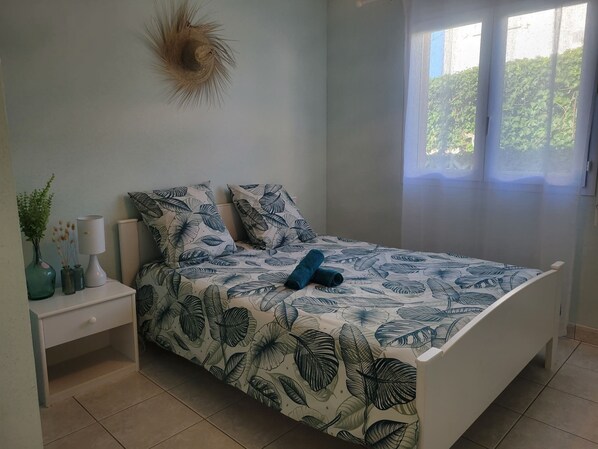 Quarto com cama, mesas de cabeceira, luminária e janela com vista para áreas verdes.