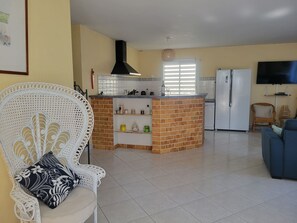 Eine Küche mit Kochinsel, einem weißen Stuhl mit gemustertem Sitzkissen, einem Fernseher und einem Kühlschrank.