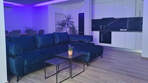 Ein modernes Wohnzimmer mit einer Eckcouch, einem Couchtisch und einer Küchenzeile mit weißen Schränken und einer schwarzen Arbeitsplatte.