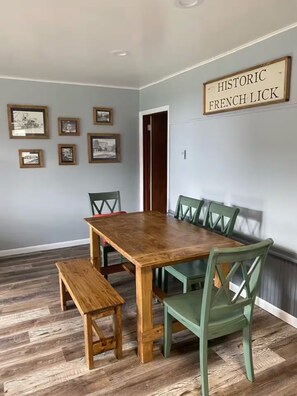 En matplats med ett träbord, tillhörande stolar och en bänk. På väggen hänger inramade tavlor och en skylt med texten ”HISTORISKA FRENCH LICK”.