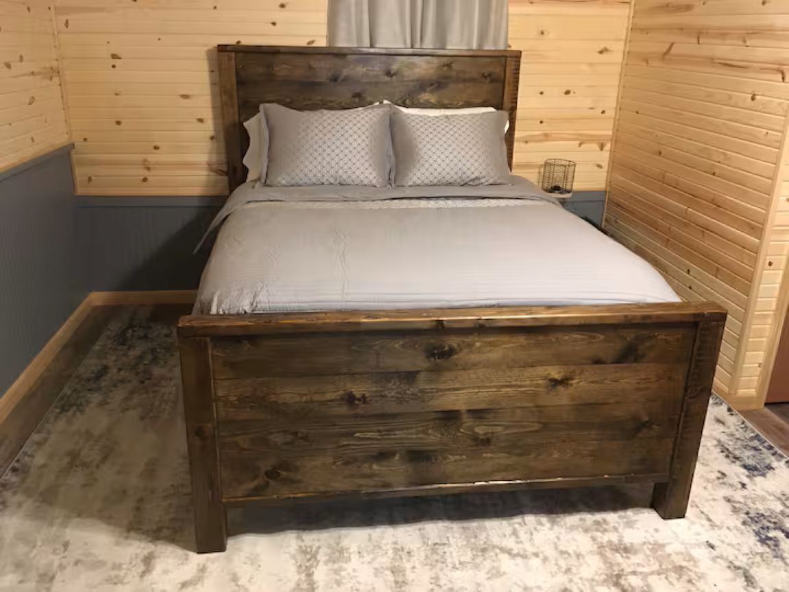 Un lit en bois avec une tête de lit, une table de chevet et une petite table de nuit, dans une pièce aux murs en bois.
