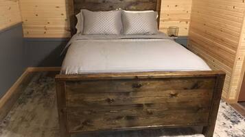 Un lit en bois avec une tête de lit, une table de chevet et une petite table de nuit, dans une pièce aux murs en bois.