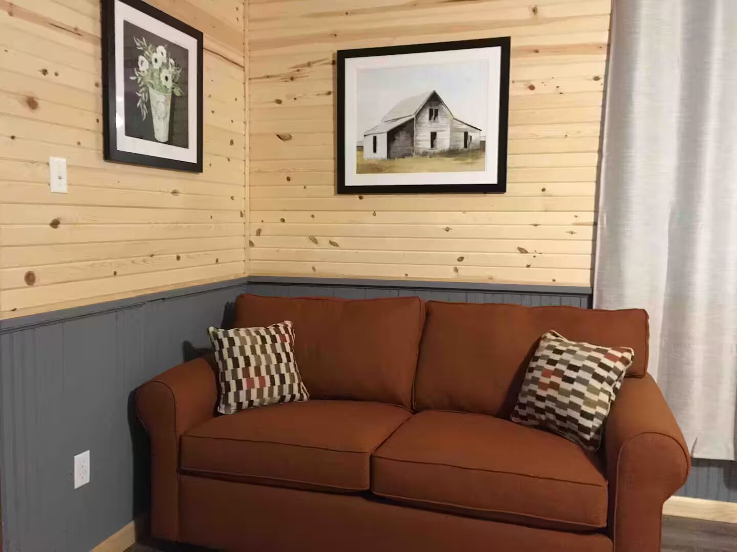 Une pièce aux murs lambrissés, avec un canapé en cuir marron, deux coussins à motifs et deux tableaux encadrés accrochés au mur.
