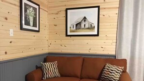 A wooden-paneled room with a brown leather sofa, two patterned pillows, and two framed pictures on the wall. - Caddy Corner has a hot tub just outside of town (French Lick)