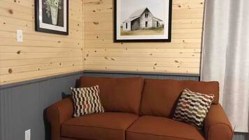 Une pièce aux murs lambrissés, avec un canapé en cuir marron, deux coussins à motifs et deux tableaux encadrés accrochés au mur.