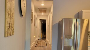 Una cocina con un refrigerador de acero inoxidable, un bote de basura y un pasillo que conduce a otra habitación.
