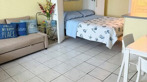 Ein kompakter Raum mit Bett, Sofa, Esstisch und Deckenventilator.