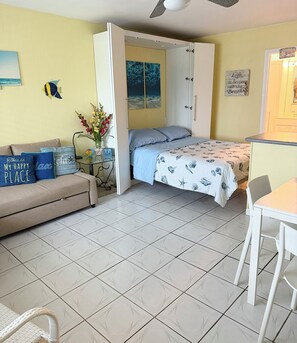 Ein kompakter Raum mit Bett, Sofa, Esstisch und Deckenventilator.