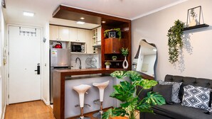 A compact living space with a kitchenette, a sofa with patterned cushions, and a potted plant. - San Isidro 635 (Santiago)