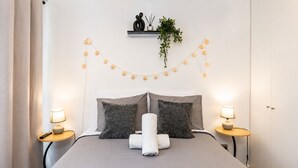 A neatly made bed with two pillows, a bedside table with a lamp, and a string of lights on the wall. - San Isidro 635 (Santiago)