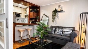 A modern living room with a sofa, two bar stools, a coffee table, and a kitchen area in the background. - San Isidro 635 (Santiago)