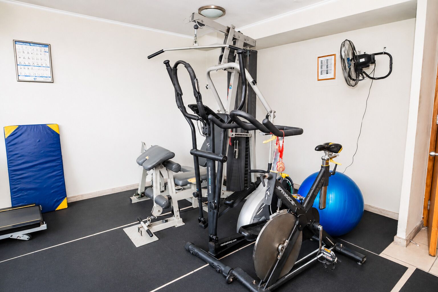 A gym with exercise equipment, a blue exercise ball, and a wall-mounted fan.