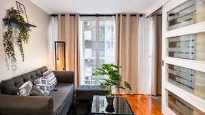 A modern living room with a sofa, a coffee table, a potted plant, and a view of the city through large windows. - San Isidro 635 (Santiago)