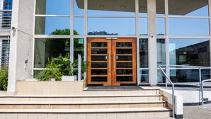 A modern building with a large glass facade, a wooden double door entrance, and a set of stairs leading up to the entrance. - San Isidro 635 (Santiago)