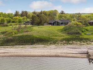 Ein modernes Haus mit großem Rasen, umgeben von üppigem Grün und einem Fluss.