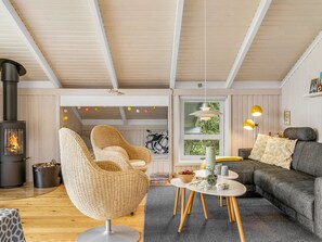 Ein gemütliches Wohnzimmer mit Kamin, Korbsesseln, einer Couch und einem Esstisch.