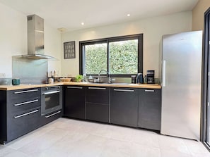 Una cocina moderna con un refrigerador de acero inoxidable, horno empotrado, un lavamanos y un ventanal con vistas a la vegetación.