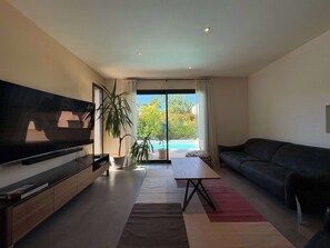 Una sala de estar moderna con una televisión de pantalla plana, un sofá, una mesa de centro y vistas a una piscina.