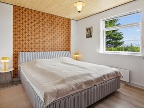 Ein Schlafzimmer mit Bett, Fenster, Lampe und Wand mit Muster.