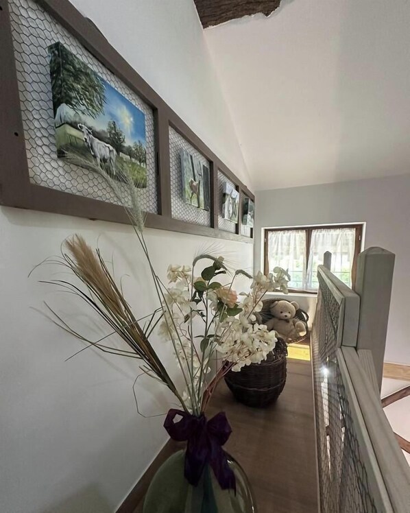 A hallway with a vase of flowers, a teddy bear, and framed pictures on the wall. - Le Clos de l'Orme - BOISSEY (BOISSEY)