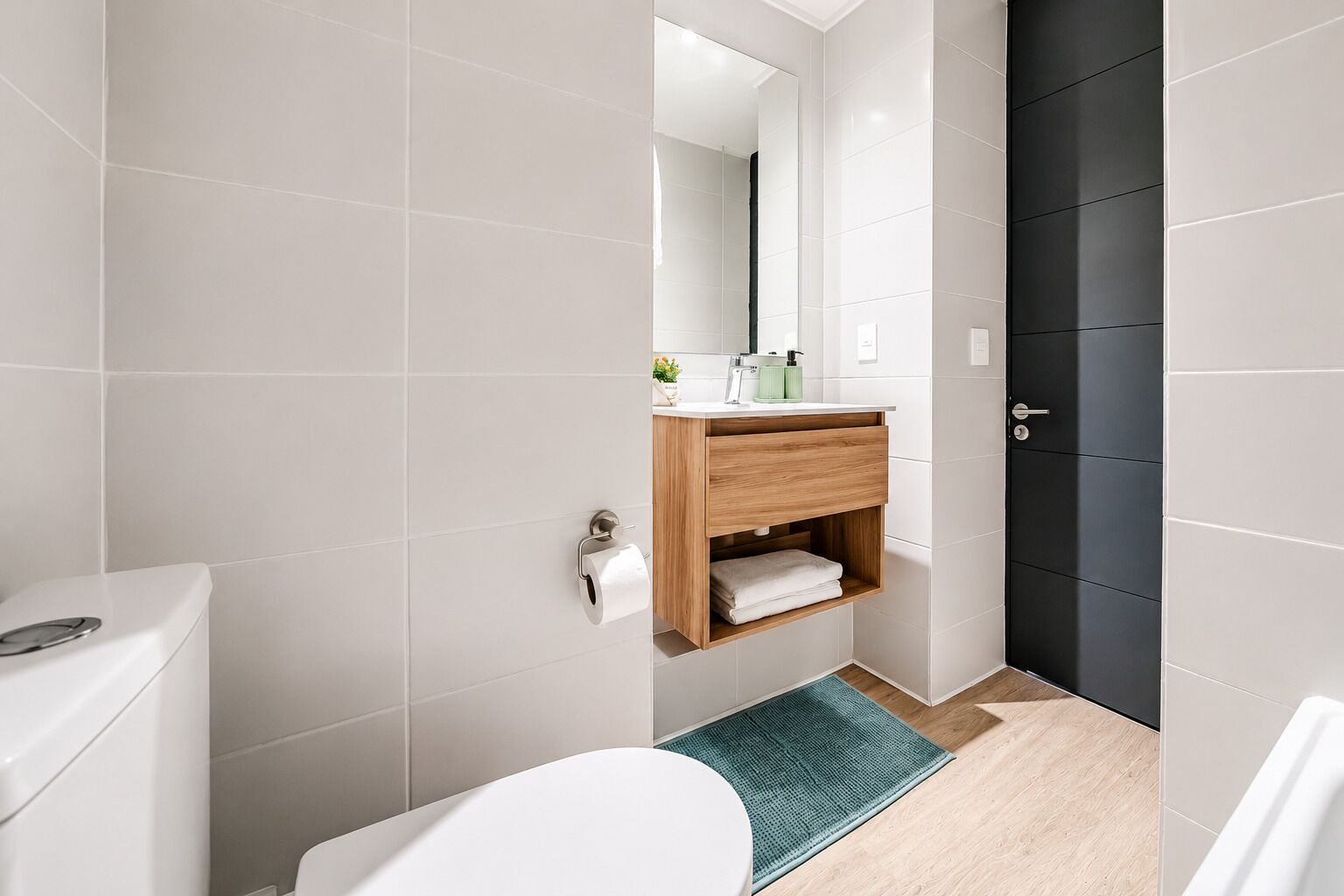 A modern bathroom with a toilet, sink, mirror, and dark door.