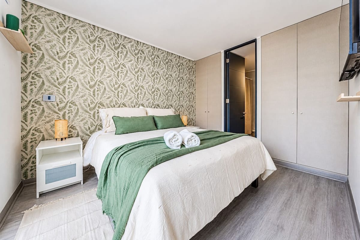 A bedroom with a bed, a nightstand, a wardrobe, and a patterned wallpaper.