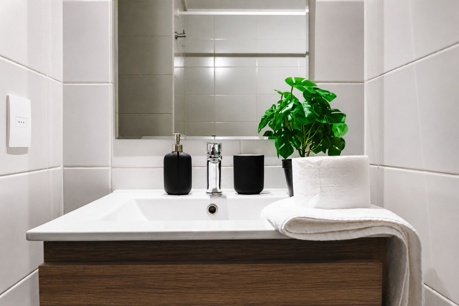 Ein Badezimmer mit einem weißen Waschbecken, zwei schwarzen Seifenspendern, einer klaren Glasseife, einem weißen Handtuch und einer grünen Pflanze in einem schwarzen Topf.