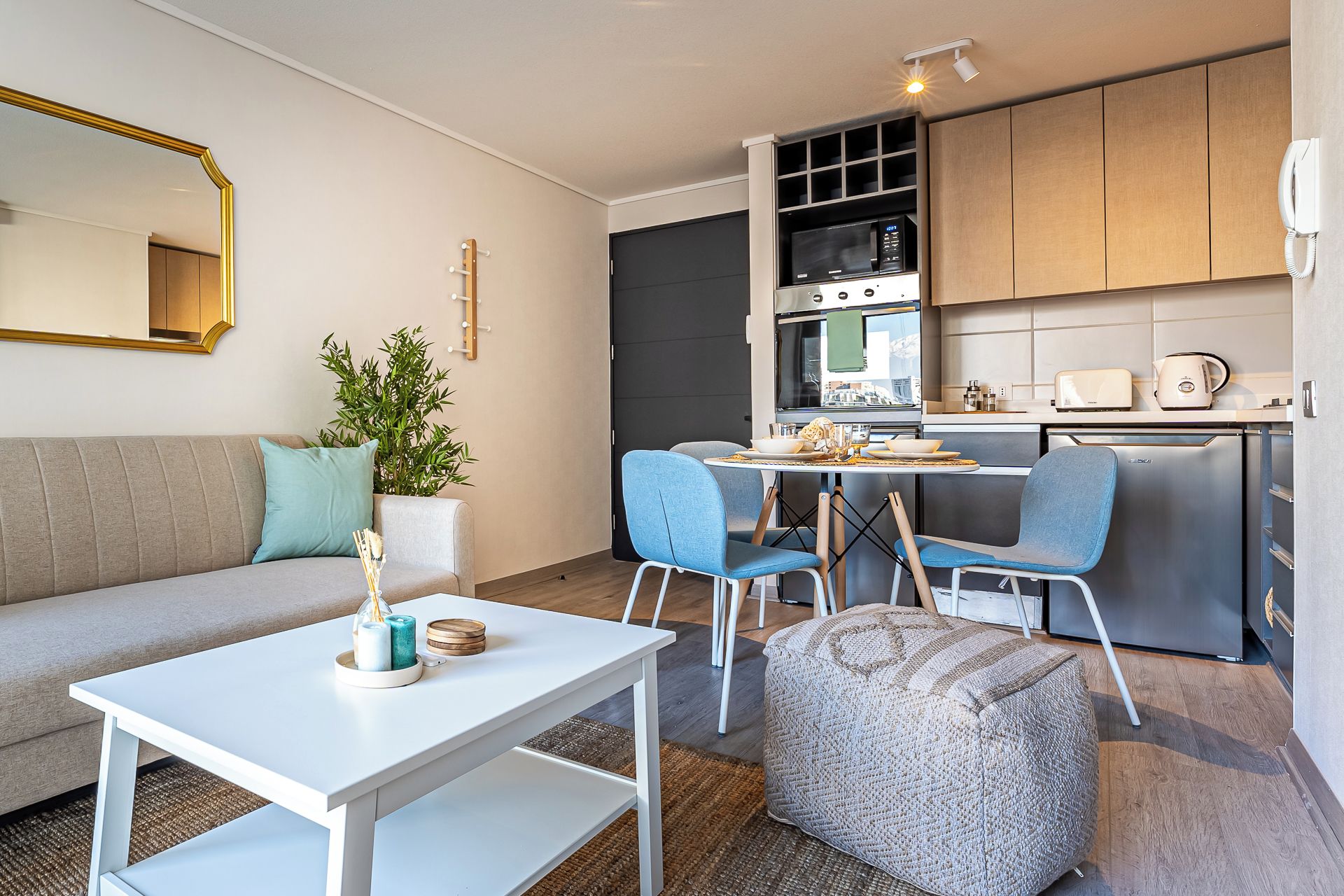 Un espacio habitable compacto con sofá, mesa de comedor, sillas, cocina equipada y un espejo grande.