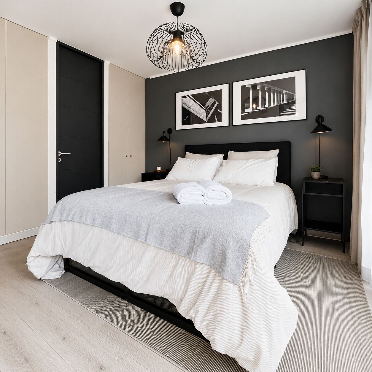 A modern bedroom with a bed, two bedside tables, a hanging light fixture, and two framed pictures on the wall.