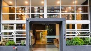 Una entrada moderna a un edificio con amplios ventanales, un acceso de vidrio y un camino que lleva al interior.