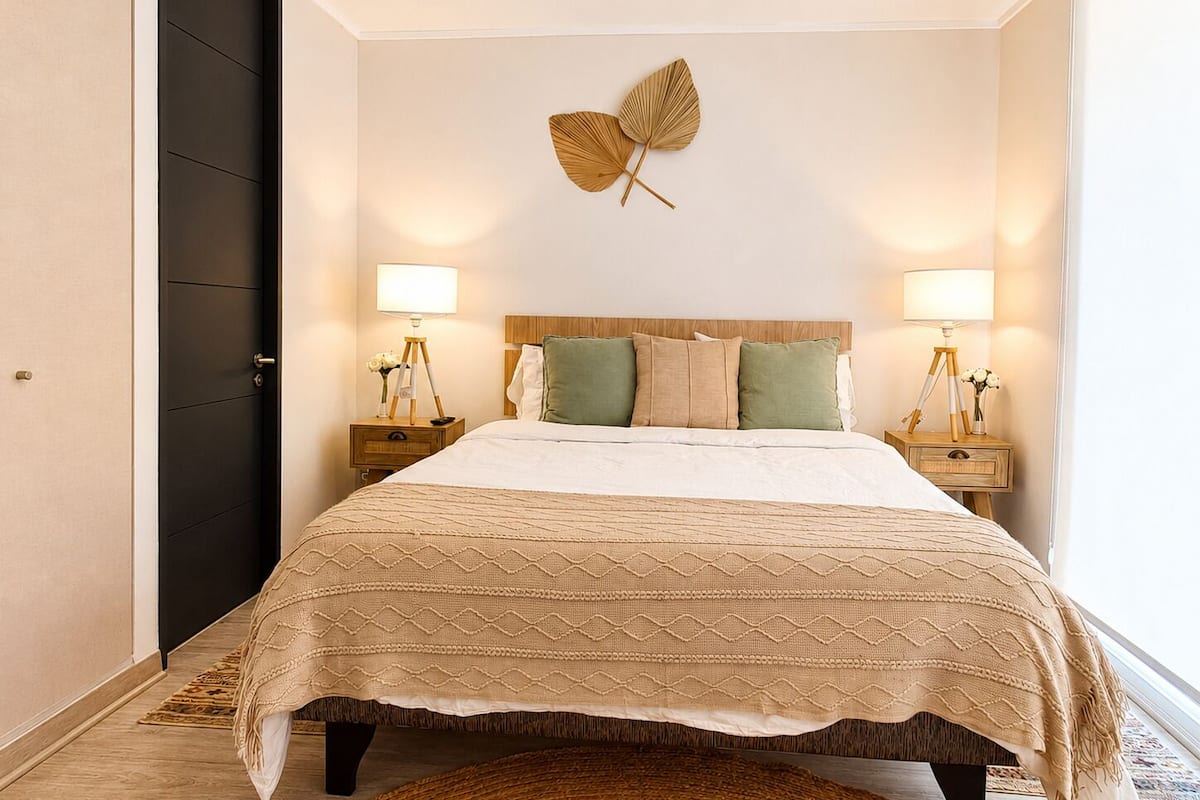 A hotel room with a bed, two bedside lamps, a wall-mounted decorative leaf, and a dark door.