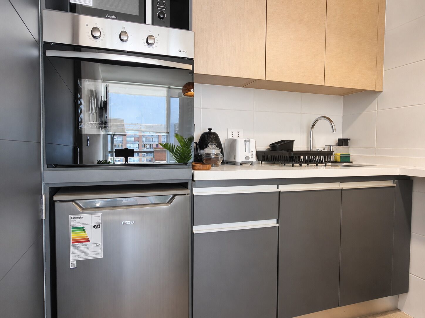 Una cocina moderna con electrodomésticos de acero inoxidable, lavavajillas y ventana con vistas a un paisaje urbano.