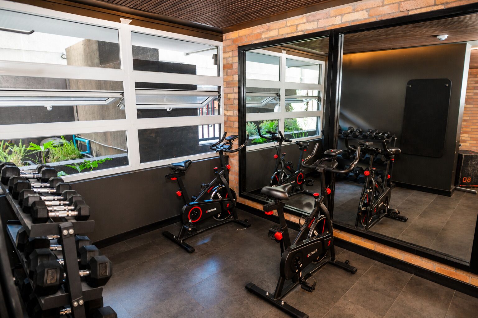 A gym with exercise bikes, dumbbells, and a large mirror reflecting the space.